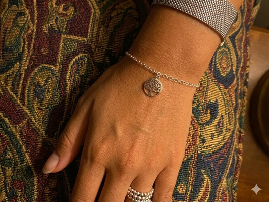 Close-up of a hand wearing a silver bracelet with a tree of life charm on a patterned fabric background.