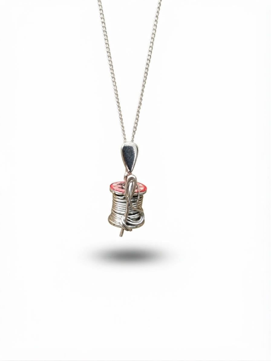 A silver wire-wrapped pendant necklace featuring a small spool design, suspended from a silver chain against a white background.