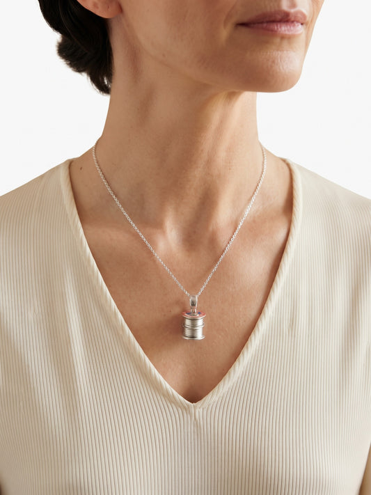 A close-up of a woman wearing a delicate silver chain necklace with a medium silver cotton reel pendant.