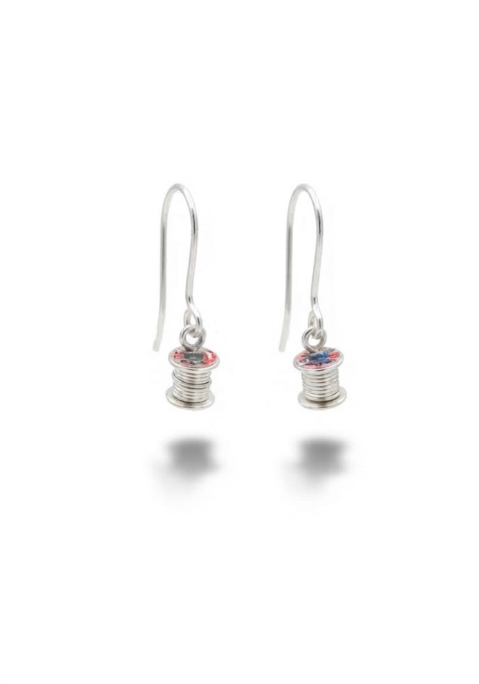 A pair of silver drop earrings featuring small cotton reel charms with red and blue enamel details, shown on a clean white background.